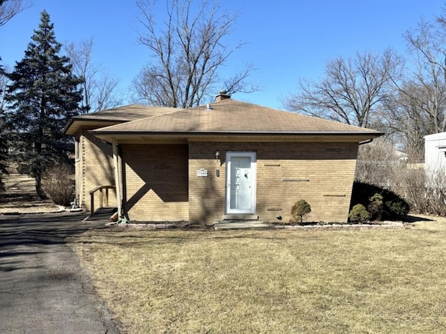 view of front of house with a front yard, brick siding, a chimney, and roof with shingles