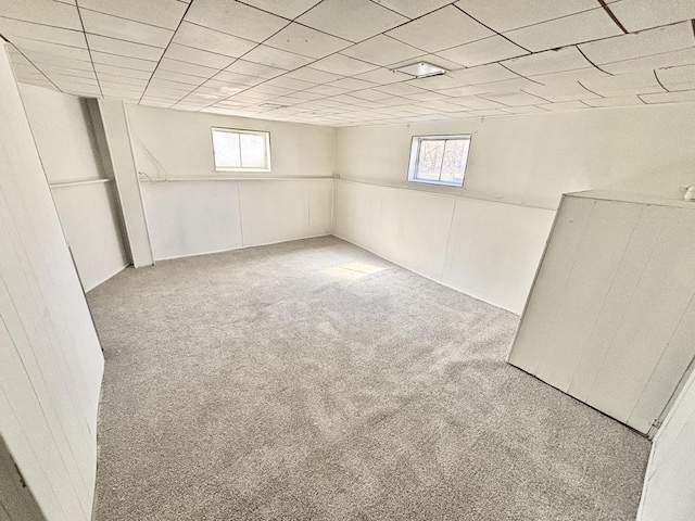 below grade area featuring carpet floors, a paneled ceiling, and wainscoting