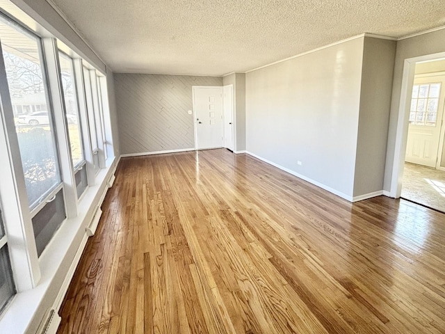 spare room with a textured ceiling, crown molding, wood finished floors, and baseboards