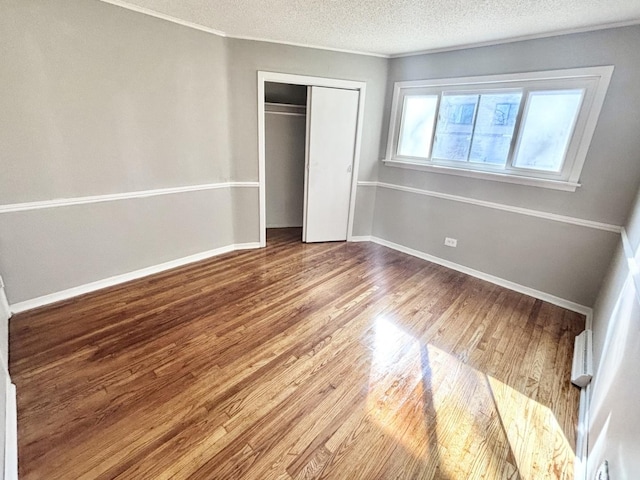 unfurnished bedroom featuring a closet, a textured ceiling, baseboards, and wood finished floors