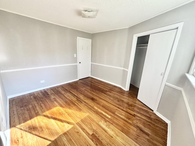 unfurnished bedroom featuring a textured ceiling, a closet, wood finished floors, and baseboards