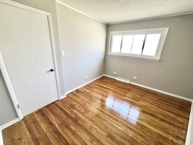 empty room featuring crown molding, a textured ceiling, baseboards, and wood finished floors