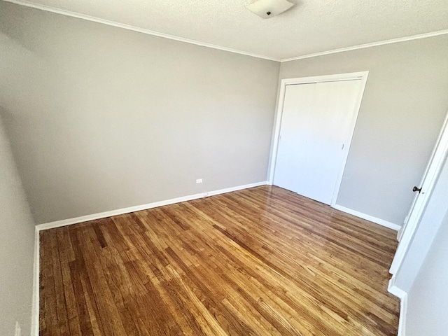 unfurnished bedroom featuring baseboards, a closet, ornamental molding, and wood finished floors