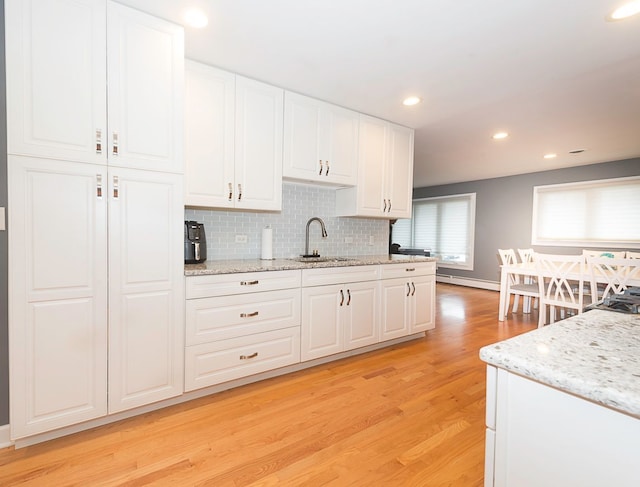 kitchen featuring light wood-style floors, backsplash, white cabinets, and a sink