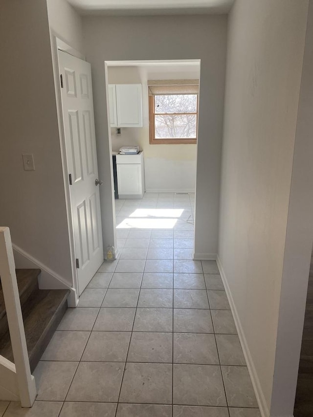 corridor featuring stairs, light tile patterned floors, and baseboards