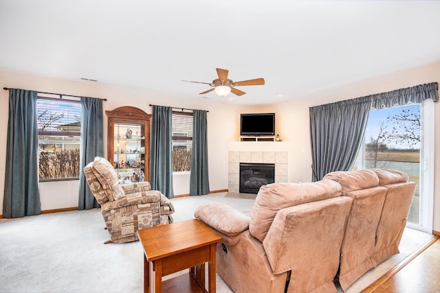 living room with a tile fireplace, light carpet, a ceiling fan, visible vents, and baseboards