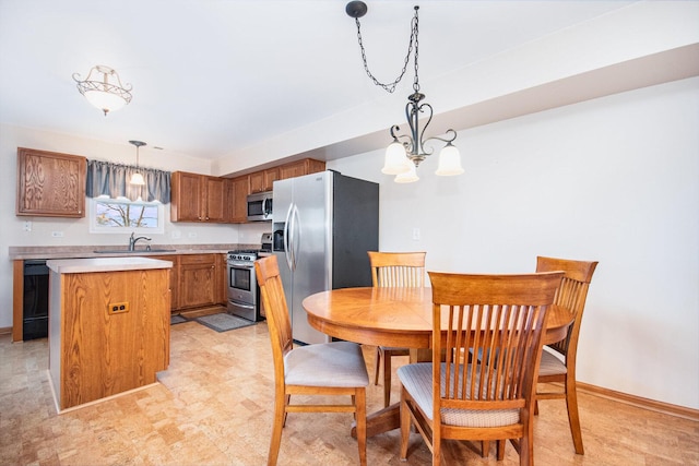 kitchen featuring brown cabinetry, hanging light fixtures, stainless steel appliances, light countertops, and a sink