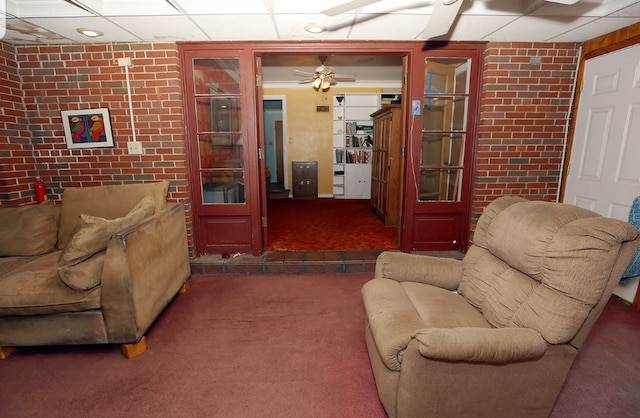 living area with carpet flooring, brick wall, ceiling fan, and a drop ceiling