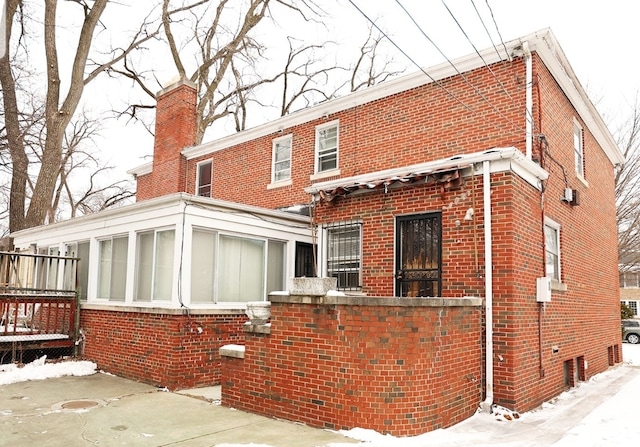 back of property with brick siding, a chimney, and a sunroom