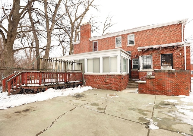 snow covered back of property featuring a patio area, brick siding, and a sunroom