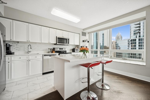 kitchen with a kitchen island, appliances with stainless steel finishes, marble finish floor, a view of city, and white cabinetry