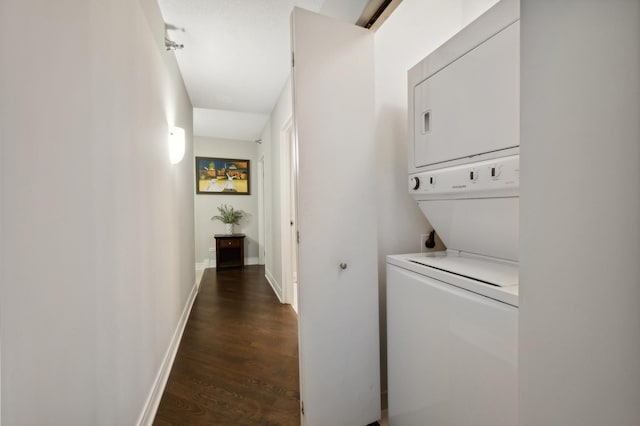 clothes washing area featuring laundry area, dark wood-type flooring, stacked washer and clothes dryer, and baseboards