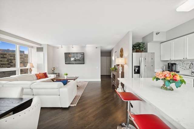 living area featuring a view of city, visible vents, dark wood-type flooring, track lighting, and baseboards