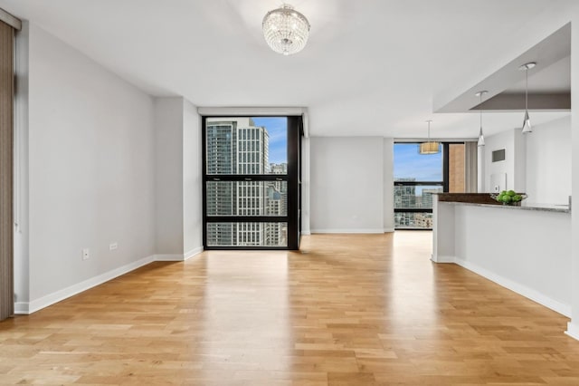 unfurnished room with baseboards, floor to ceiling windows, light wood finished floors, and an inviting chandelier