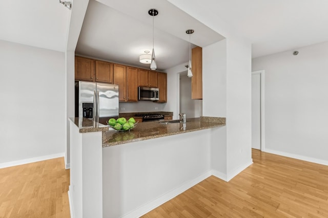 kitchen with a peninsula, a sink, hanging light fixtures, appliances with stainless steel finishes, and brown cabinets