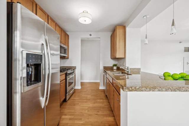 kitchen featuring light wood-style flooring, a sink, hanging light fixtures, appliances with stainless steel finishes, and brown cabinetry