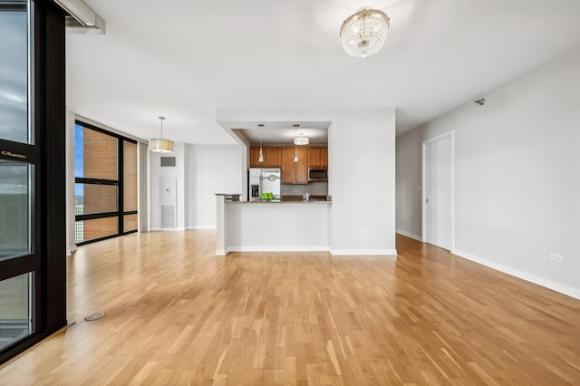 unfurnished living room featuring baseboards, light wood-type flooring, an inviting chandelier, and floor to ceiling windows