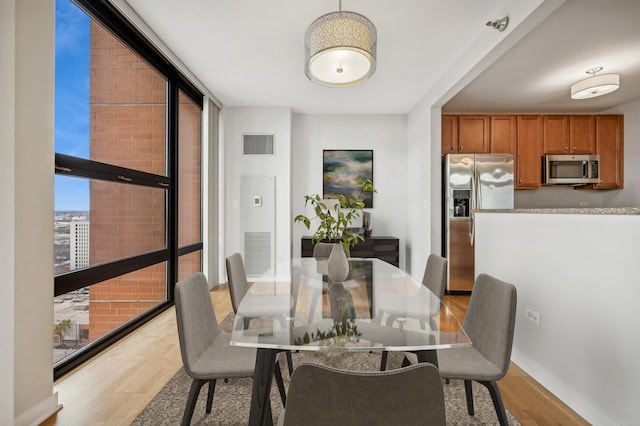 dining room featuring baseboards, floor to ceiling windows, visible vents, and light wood finished floors