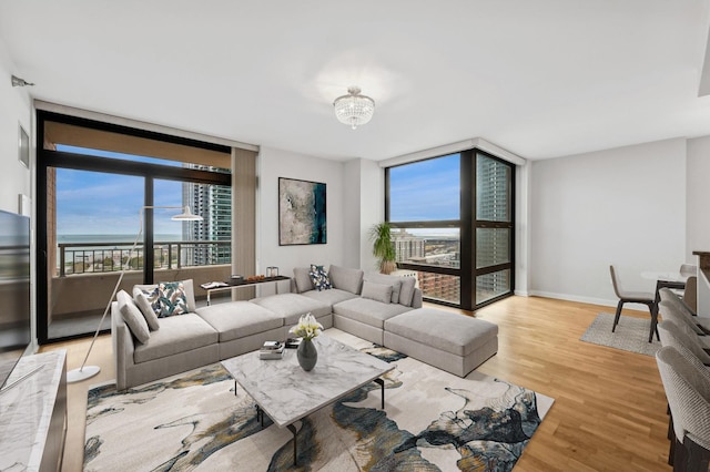 living room with baseboards, light wood-type flooring, a water view, and floor to ceiling windows