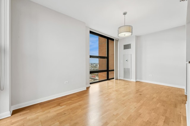 spare room featuring a wall of windows, baseboards, visible vents, and light wood finished floors