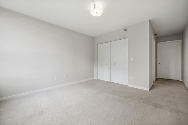 unfurnished bedroom with a closet, light colored carpet, and baseboards