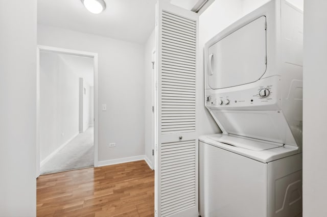 laundry room with laundry area, light wood finished floors, stacked washer / dryer, and baseboards