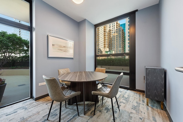 dining room with light wood finished floors, baseboards, floor to ceiling windows, and a city view