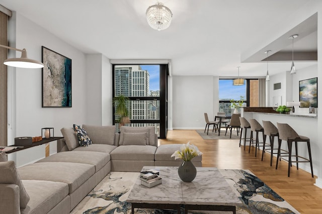 living room with light wood-type flooring, an inviting chandelier, expansive windows, and baseboards