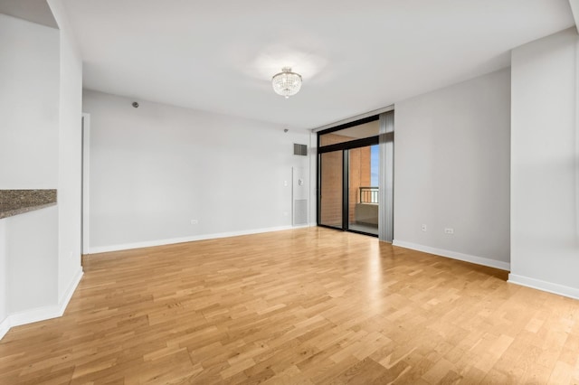 empty room with a wall of windows, light wood-type flooring, visible vents, and baseboards