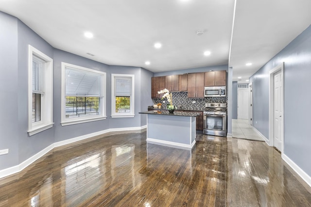 kitchen with a kitchen island, baseboards, appliances with stainless steel finishes, tasteful backsplash, and dark countertops