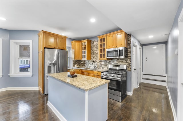 kitchen featuring a kitchen island, glass insert cabinets, light stone countertops, stainless steel appliances, and a sink