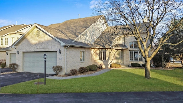 view of front of home featuring aphalt driveway, brick siding, a shingled roof, a front yard, and a garage