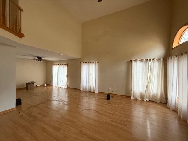 unfurnished living room featuring ceiling fan, light wood finished floors, plenty of natural light, and a high ceiling