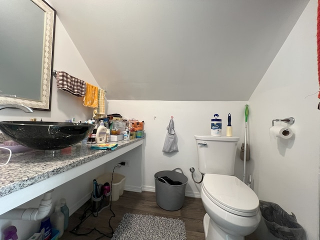 half bathroom with toilet, vaulted ceiling, vanity, wood finished floors, and baseboards