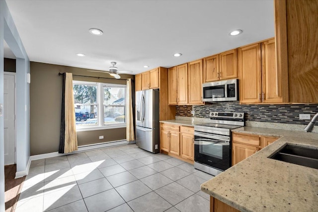 kitchen with light tile patterned floors, appliances with stainless steel finishes, a sink, light stone countertops, and backsplash