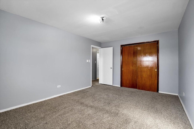 unfurnished bedroom with dark colored carpet, a closet, and baseboards