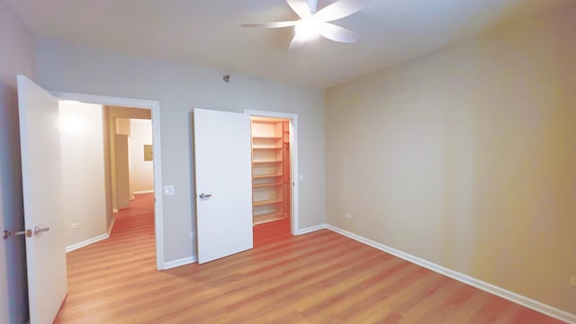 unfurnished bedroom featuring baseboards, a ceiling fan, a spacious closet, light wood-type flooring, and a closet