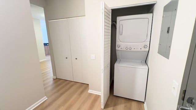 laundry area featuring laundry area, electric panel, baseboards, stacked washer and clothes dryer, and light wood-style floors