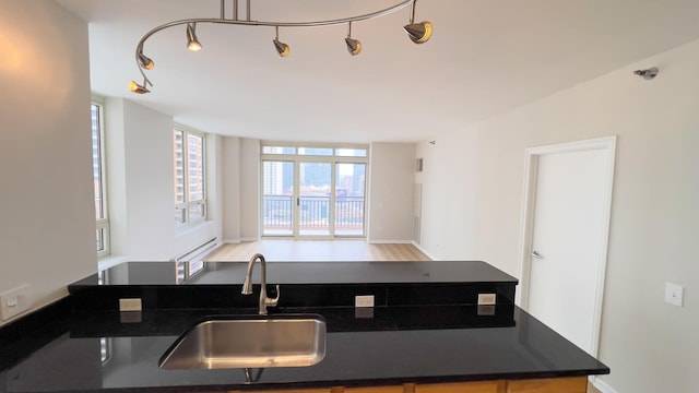 kitchen featuring dark countertops, a wall of windows, a sink, and wood finished floors