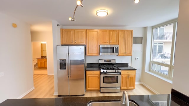 kitchen featuring baseboards, dark countertops, stainless steel appliances, light wood-style floors, and a sink