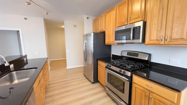 kitchen featuring appliances with stainless steel finishes, dark stone counters, a sink, light wood-type flooring, and baseboards