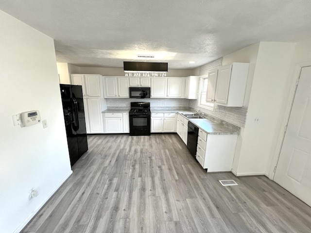 kitchen featuring light wood finished floors, white cabinets, a sink, black appliances, and backsplash