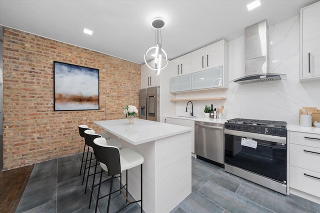 kitchen featuring brick wall, a kitchen island, stainless steel appliances, wall chimney range hood, and a sink