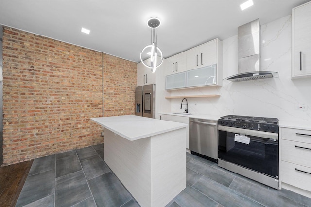 kitchen featuring light countertops, appliances with stainless steel finishes, a sink, wall chimney range hood, and brick wall