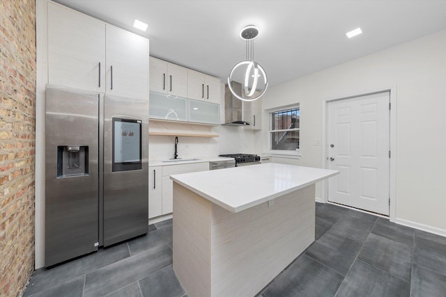 kitchen with stainless steel appliances, light countertops, a sink, a kitchen island, and brick wall