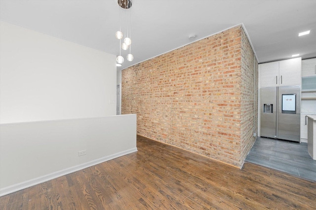 spare room with brick wall, wood finished floors, and baseboards