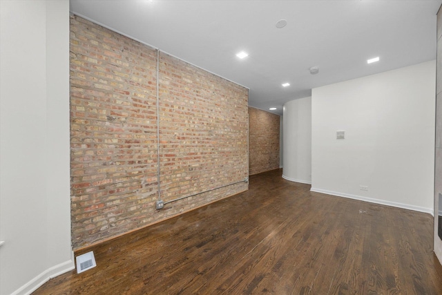 spare room featuring brick wall, wood finished floors, visible vents, and baseboards