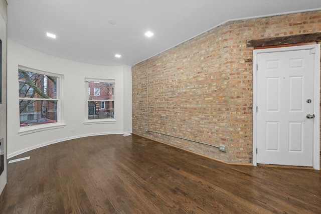 empty room with brick wall, baseboards, and wood finished floors