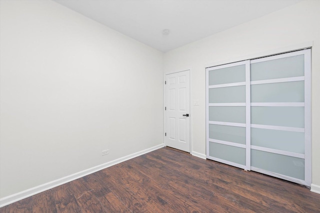 unfurnished bedroom with a closet, dark wood-style flooring, and baseboards