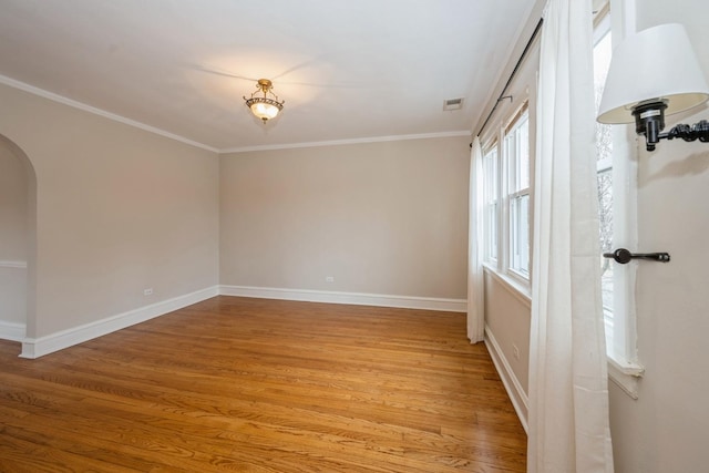 spare room with arched walkways, light wood finished floors, visible vents, ornamental molding, and baseboards